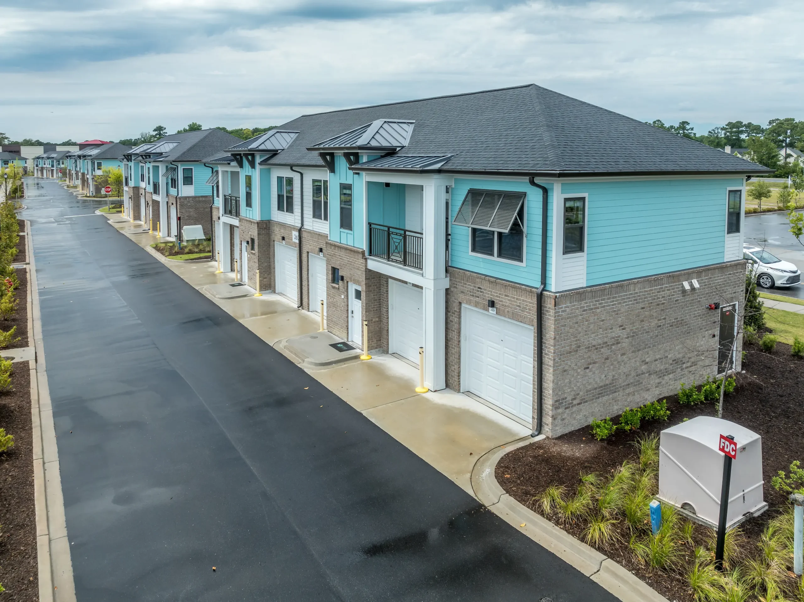 Multi-family rental property with grey brick and alternating blue & white siding on a wet road